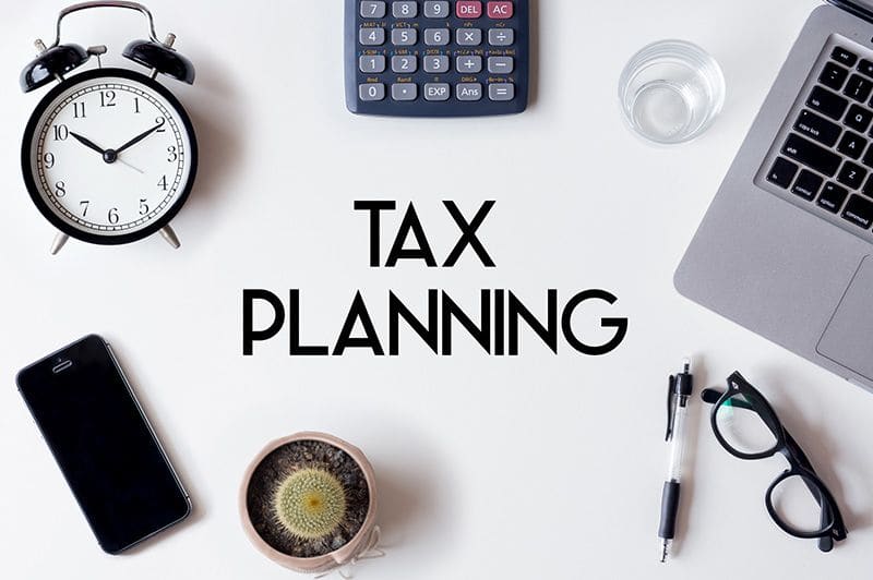 Desk with a clock, calculator and a note reading Tax Planning